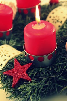 A red candle burning brightly on a decorative Christmas wreath with festive ornaments.